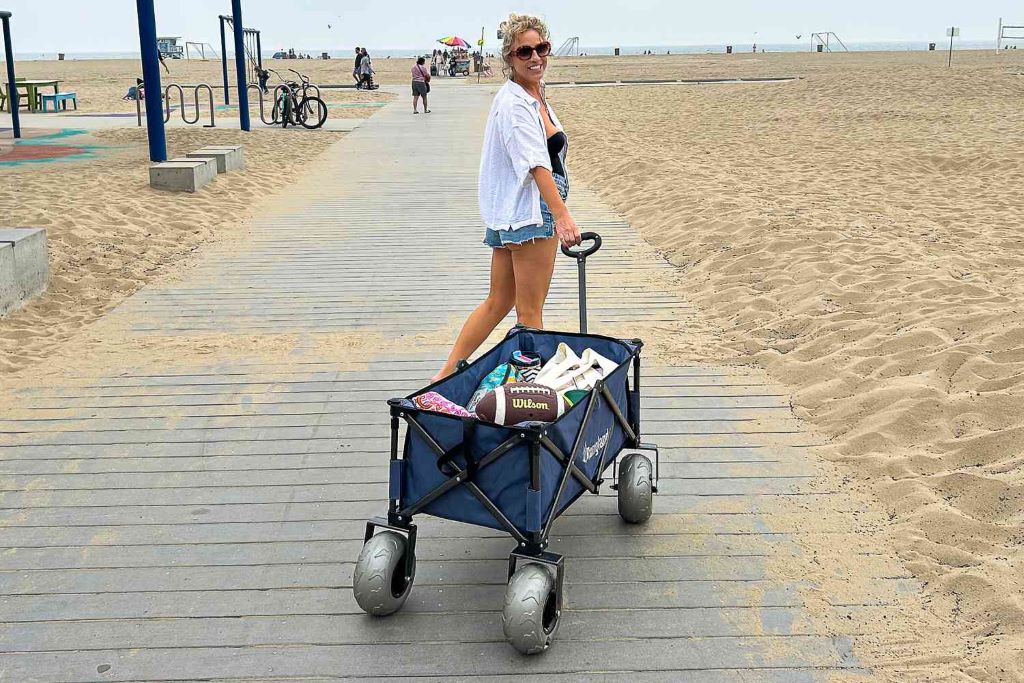 Foldable beach wagon cart loaded with beach gear being pulled across sandy shore