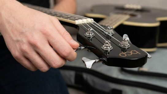 Player tuning a Choice Products bass guitar with electronic tuner